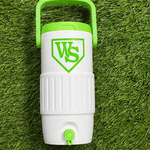 May include: White and green water cooler with a green handle and a green logo. The cooler has a white body with a green lid and a green spigot. The logo is a green "WS" inside a green baseball-shaped emblem.