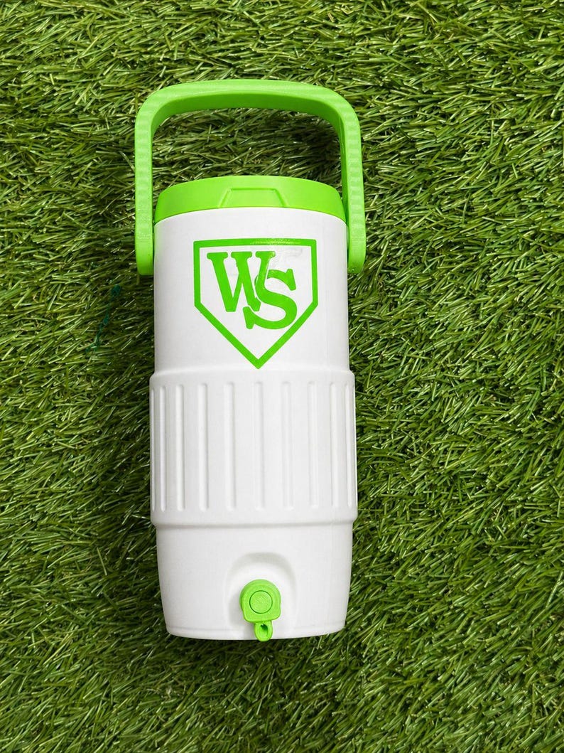 May include: White and green water cooler with a green handle and a green logo. The cooler has a white body with a green lid and a green spigot. The logo is a green "WS" inside a green baseball-shaped emblem.
