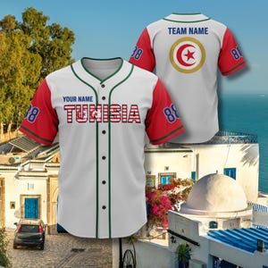 K&ouml;nnte beinhalten: Wei&szlig;es Baseball-Trikot mit roten &Auml;rmeln und gr&uuml;nen Zierleisten. Das Trikot zeigt das Wort "TUNISIA" in Rot und Wei&szlig;, mit der Nummer "88" auf den &Auml;rmeln. Auf der R&uuml;ckseite des Trikots befindet sich ein kreisf&ouml;rmiges Emblem mit einem roten Stern.