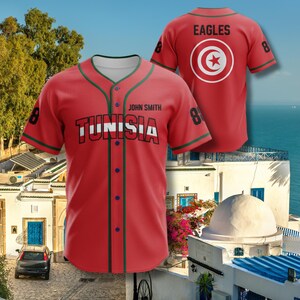 K&ouml;nnte beinhalten: Rotes Baseball-Trikot mit "TUNISIA" in wei&szlig;en Blockbuchstaben auf der Brust. Das Trikot hat gr&uuml;ne und blaue Akzente, die Nummer 8 auf den &Auml;rmeln und den Namen "John Smith" &uuml;ber dem Teamnamen. Auf der R&uuml;ckseite des Trikots steht "EAGLES" und es hat ein kreisf&ouml;rmiges Emblem.