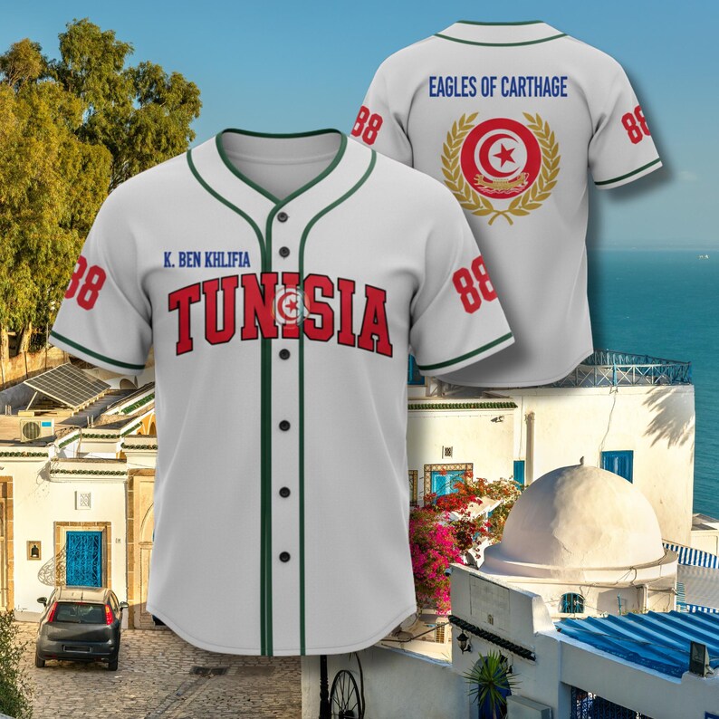 K&ouml;nnte beinhalten: Wei&szlig;es Baseball-Trikot mit gr&uuml;nen Zierleisten, dem Wort "TUNISIA" in Rot und der Nummer 88 auf den &Auml;rmeln. Auf der R&uuml;ckseite des Trikots steht "EAGLES OF CARTHAGE" und ein kreisf&ouml;rmiges Emblem.