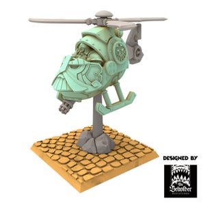 May include: A green and gray miniature helicopter with a dwarf pilot. The helicopter is on a stand with a stone base and a cobblestone surface. The text "DESIGNED BY The Beholder Miniatures" is in the lower right corner of the image.