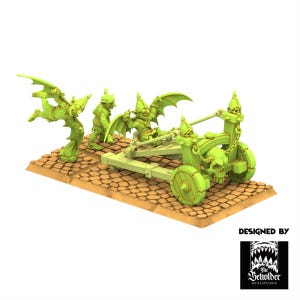 Peut inclure: Une catapulte miniature vert clair avec des figurines de gobelins. La catapulte présente un design de crâne et repose sur une base marron texturée. Les gobelins ont des ailes de chauve-souris et des oreilles pointues. L'image comprend le texte "DESIGNED BY" et un logo.