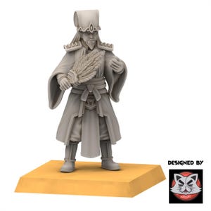 Peut inclure: Figurine grise claire d'une figure vêtue d'une robe tenant un éventail et un petit objet. La figurine se tient sur une base rectangulaire jaune. La figurine a une longue barbe et un grand chapeau. Les mots "DESIGNED BY" et un logo sont dans le coin inférieur droit.