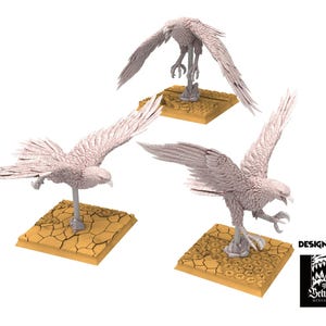Puede incluir: Tres miniaturas detalladas de águilas de color claro en varias poses de vuelo. Cada águila está montada sobre una base cuadrada y texturizada. La imagen incluye el texto "DESIGNED BY" y un logotipo de "The Beholder Miniatures".