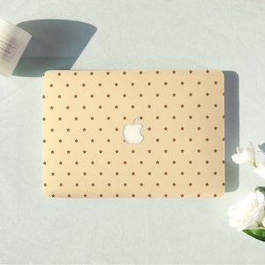 May include: A beige laptop case with a repeating pattern of small brown stars. The case has a cutout for the Apple logo. The laptop case is on a light blue surface.