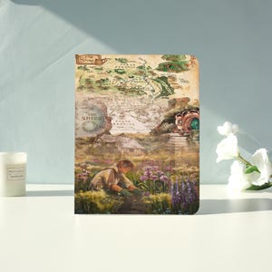 May include: A decorative tablet case featuring a map of The Shire from The Lord of the Rings. The case has a vintage aesthetic with a detailed map design, a hobbit hole, and a person tending a garden. The text "The Shire" is visible.
