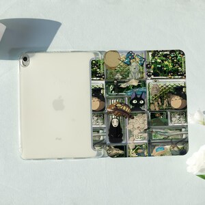 May include: Clear iPad case featuring a colorful anime-style design. The case has a grid-like pattern with various characters and scenes. The iPad is visible through the clear case, showing the Apple logo.