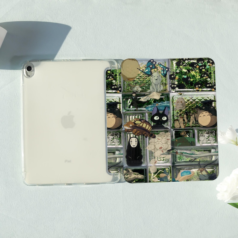 May include: Clear iPad case featuring a colorful anime-style design. The case has a grid-like pattern with various characters and scenes. The iPad is visible through the clear case, showing the Apple logo.