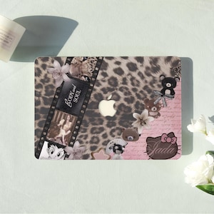 May include: A decorative laptop cover featuring a leopard print design with a film strip, floral accents, and cartoon characters. The cover includes the text "Body and Soul" and a Hello Kitty design with the name "Jada".