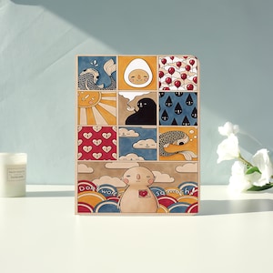 May include: A rectangular notebook featuring a grid of colorful illustrations including a fish, an egg, balloons, a sun, a dark figure with a bowl, raindrops, hearts, clouds, and a central character with the text "Don't worry so much!" printed below.