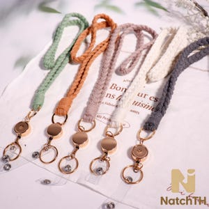 May include: Five woven lanyards in shades of green, orange, mauve, cream, and gray. Each lanyard has a gold-colored metal badge reel and key ring. The lanyards are displayed on a white surface with text.