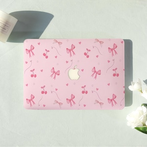 May include: Pink laptop case with a pattern of pink bows, cherries, and hearts. The case has a cutout for the Apple logo. The design is repeated across the surface of the case.