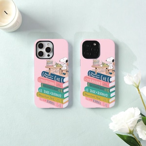 May include: Two light pink phone cases featuring a graphic of Snoopy sitting at a desk with a stack of books. The books are titled Pride and Prejudice, Persuasion, Northanger Abbey, Sense and Sensibility, Mansfield Park, and Emma by Jane Austen.