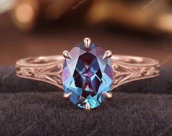 May include: A rose gold ring featuring an oval-cut color-changing gemstone that shifts between blue and purple hues. The band is crafted with intricate floral-inspired engravings along the shoulders, held by six prongs in a classic setting.