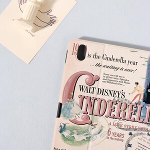 May include: A light pink tablet case featuring a vintage-style illustration of Walt Disney's Cinderella. The design includes text that reads "1950 is the Cinderella year" and "A love story with 6 years in the making."