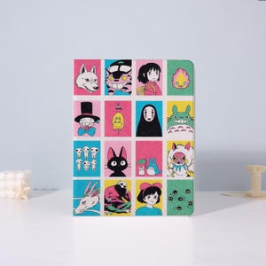 May include: A colorful square notebook featuring a grid of cartoon character illustrations. Each square showcases a different character in vibrant colors, including a white wolf, a black cat, and a girl with a pink bow. The notebook is on a white surface.