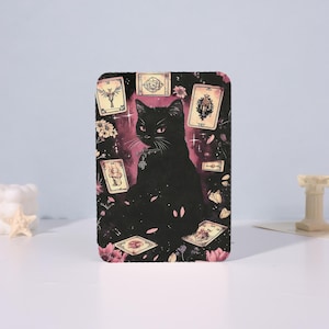 May include: A rectangular black cat design with tarot cards and floral accents. The image features a black cat with red eyes, surrounded by floating tarot cards and pink flowers against a dark pink background. The design is likely for a phone case or similar item.