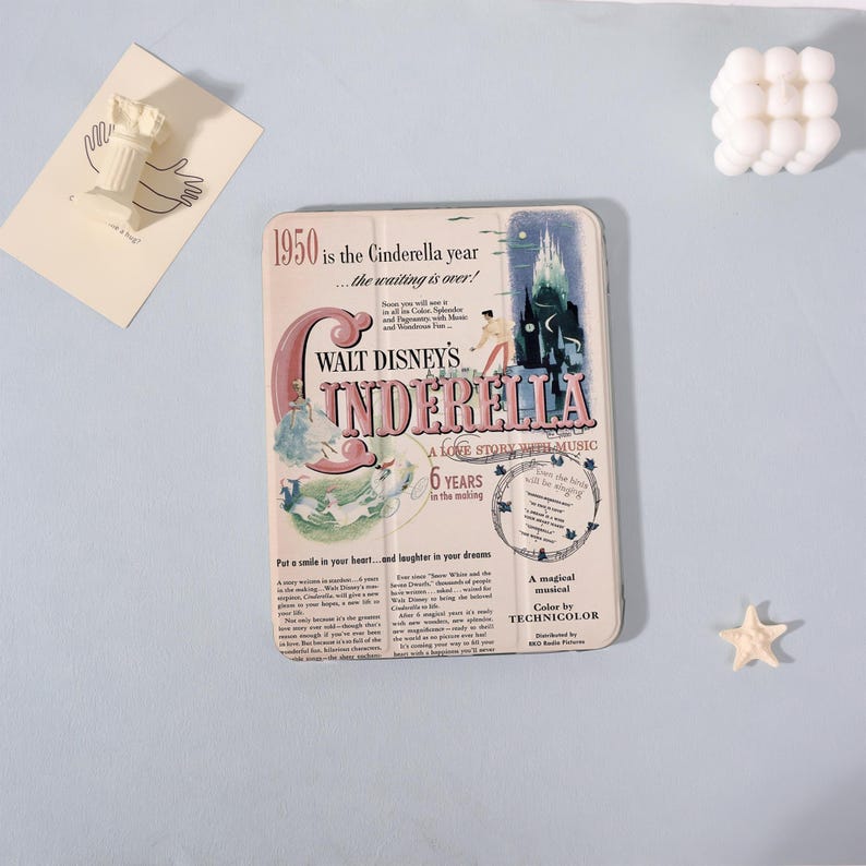 May include: A rectangular, vintage-style Cinderella-themed decorative item. The design features the text "WALT DISNEY'S CINDERELLA" with illustrations and the text "1950 is the Cinderella year...the waiting is over!"