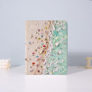 May include: A rectangular artwork showing a beach scene with tiny figures, colourful umbrellas, and textured waves. The art piece features a sandy shore and turquoise water, creating a detailed coastal landscape.