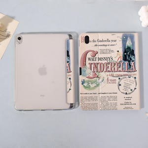 May include: A clear iPad with a case featuring a vintage-style "Cinderella" movie poster design. The poster has a pink and blue color scheme with text that reads "Walt Disney's Cinderella" and "A Love Story With Music."