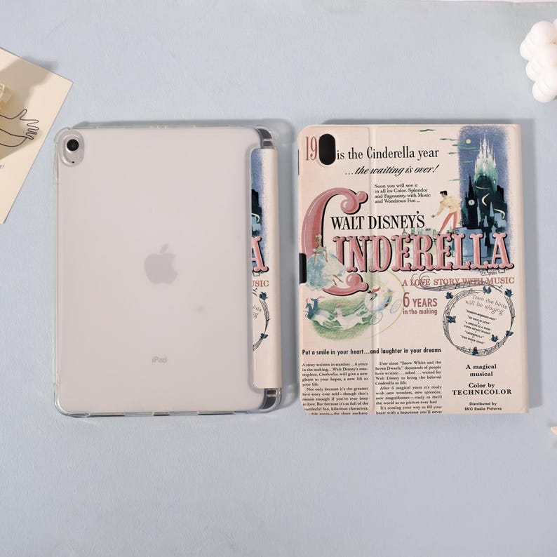 May include: A clear iPad with a case featuring a vintage-style "Cinderella" movie poster design. The poster has a pink and blue color scheme with text that reads "Walt Disney's Cinderella" and "A Love Story With Music."