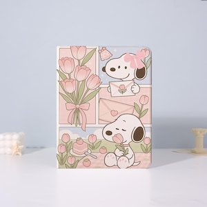 Könnte beinhalten: Eine hellrosa und weiß illustrierte Hülle mit Snoopy, Tulpen, einem Kuchen und Umschlägen. Snoopy wird mit einer Blume und einer rosa Schleife gezeigt. Die Hülle hat ein Comic-Design mit hellrosa Hintergrund.