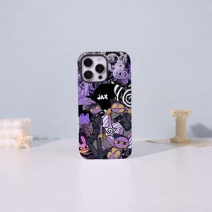 May include: A purple and black phone case featuring a collage of cartoon characters, including a rabbit-like figure in a dark uniform, the name JAX, and various abstract patterns, spirals, and stars printed across the entire surface of the case.