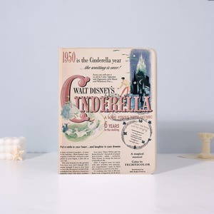Peut inclure: Une couverture de livre de style vintage pour Cendrillon de Walt Disney, avec le titre en grandes lettres roses. La couverture comprend des illustrations de Cendrillon, un château et le texte "A Love Story with Music" et "Color by Technicolor".