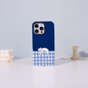 Peut inclure: Une coque de smartphone bleu foncé avec une illustration de chat blanc reposant sur un motif à carreaux bleu clair et blanc. La coque présente une découpe pour les objectifs de l'appareil photo en haut à gauche, offrant une protection mobile.