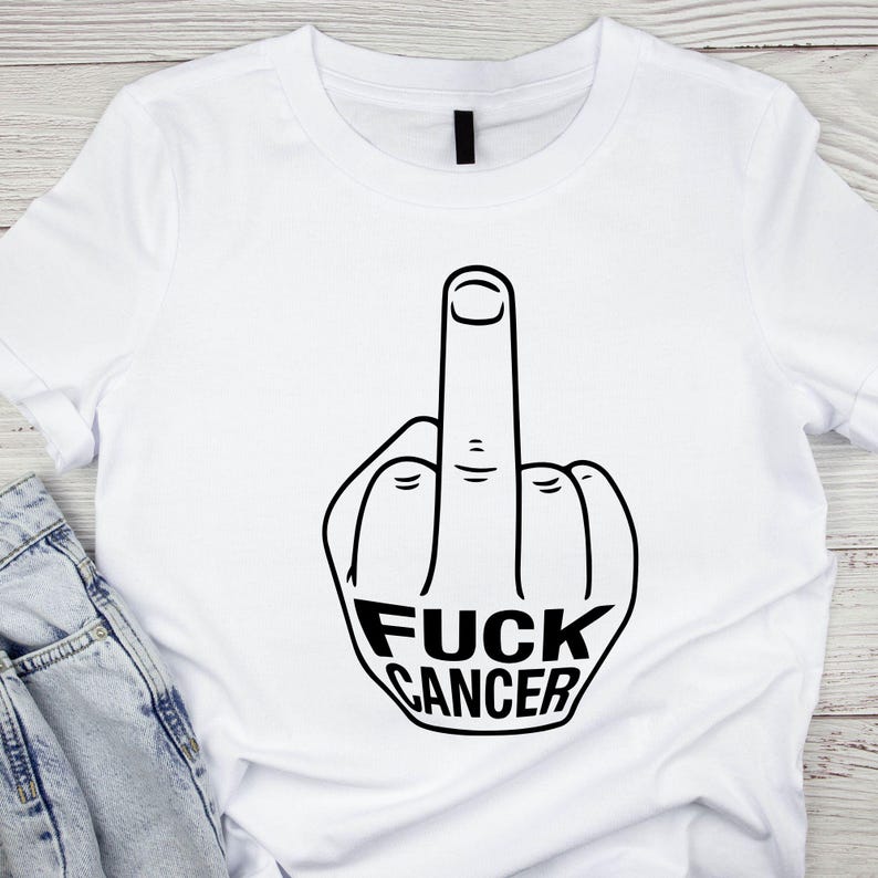 May include: White t-shirt with a black graphic of a hand giving the middle finger. The text "FUCK CANCER" is printed in bold, black letters below the hand gesture. The shirt is made of a soft material.