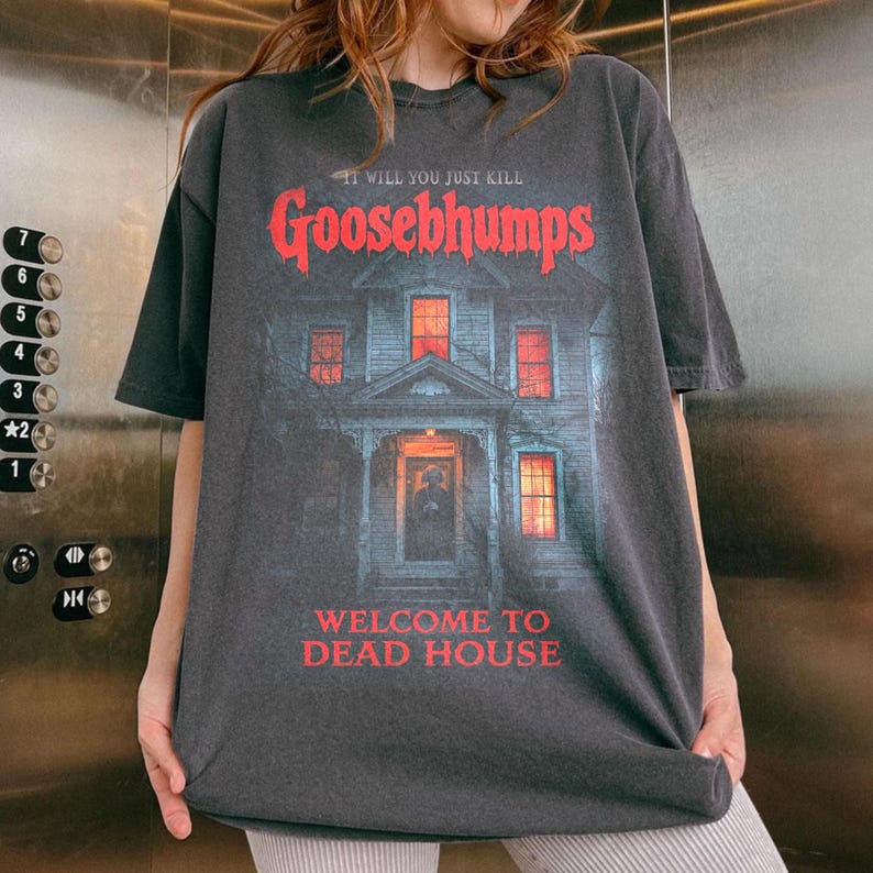 May include: Dark grey Goosebumps t-shirt with a haunted house graphic and red text: "IT WILL YOU JUST KILL Goosebumps WELCOME TO DEAD HOUSE". The tee has a vintage, worn appearance.