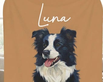 May include: A tan blanket with a black and white Border Collie dog portrait and the name "Luna" in cursive. The dog is depicted with its tongue out. The blanket is held up in front of a person.