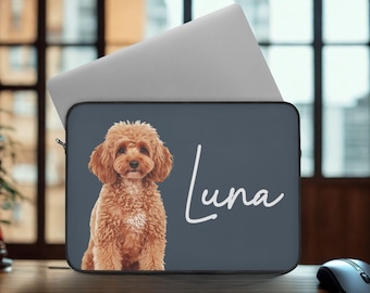 May include: A laptop sleeve featuring a portrait of a brown poodle with the name "Luna" in white script on a dark gray background. A silver laptop is partially visible behind the sleeve. The sleeve is on a wooden desk.