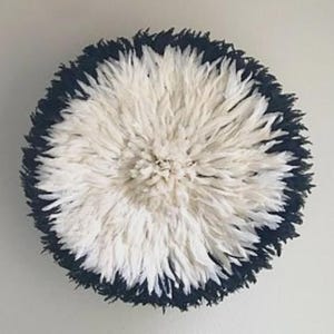 May include: Round wall decor featuring a central cluster of white feathers surrounded by a border of dark blue feathers. The decorative piece is mounted on a light-colored wall, creating a striking contrast.