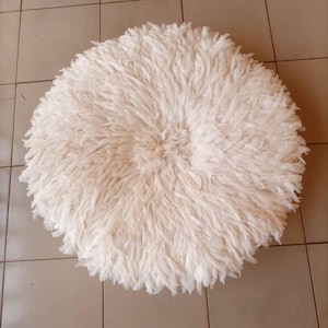 May include: A round, off-white decorative item with a dense, fluffy texture. The item appears to be made of soft, feathery material, possibly feathers or a similar textile. The shape is circular, and the overall appearance is plush and inviting.