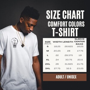 May include: A white t-shirt with a small black lightbulb graphic on the chest. Next to the shirt is a size chart for Comfort Colors t-shirts, listing sizes S through 3XL with width, length, and sleeve center back measurements in inches.