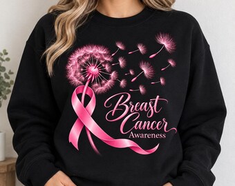 May include: A black long-sleeve sweatshirt featuring a graphic print of a pink dandelion with seeds blowing away. A pink awareness ribbon is intertwined with the dandelion stem. The text Breast Cancer Awareness is printed in pink script.