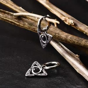 May include: A pair of silver hoop earrings with a triangular pendant featuring a black stone and intricate Celtic knotwork design.