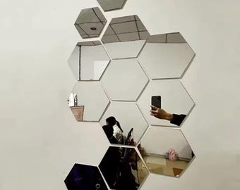 May include: A set of nine hexagonal mirrors in various sizes, arranged in a honeycomb pattern on a white wall. The mirrors are reflective and show a reflection of a person and a room.