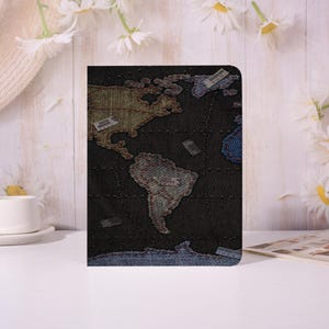 May include: A dark denim-textured notebook cover featuring a world map design. The map is stitched with various colored threads, highlighting continents and countries. The cover has a stitched border and includes labels for continents.