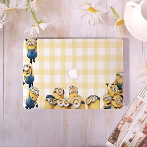 May include: Yellow and white checkered laptop case featuring a group of Minions characters. The case has a white Apple logo and is decorated with various Minions in blue overalls and goggles.