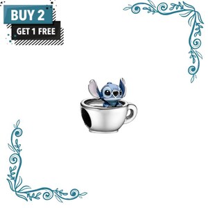May include: A silver-toned metal charm featuring a blue character with large ears sitting inside a small cup. The image includes text that reads BUY 2 GET 1 FREE in a black and blue box. The charm has a polished finish and a handle on the side.