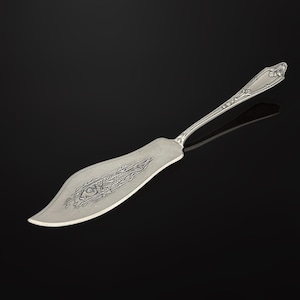 May include: A silver fish server with a decorative handle and a wide, curved blade. The blade features an etched design of a fish. The server is made of a shiny, reflective metal and is set against a black background.