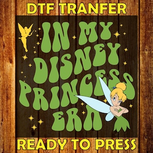 May include: A DTF transfer design with the text "IN MY DISNEY PRINCESS ERA" in green, featuring Tinkerbell and a fairy silhouette. The design is on a dark wood-grain background with the words "READY TO PRESS".