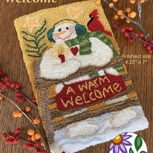 Puede incluir: Un patrón de aguja de punzón que presenta un muñeco de nieve sosteniendo un corazón y una vela, con un cardenal y una estrella en el fondo. El patrón se titula "A Warm Welcome" y mide 10,8 cm por 17,8 cm.