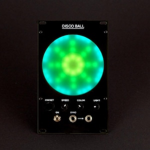Può includere: Dispositivo elettronico nero con la scritta "DISCO BALL" in alto. Un grande cerchio verde brillante domina il centro. Sotto ci sono i controlli etichettati "PRESET", "SPEED", "COLOR" e "LIGHT", insieme a un interruttore "ON" e porte "SYNC".