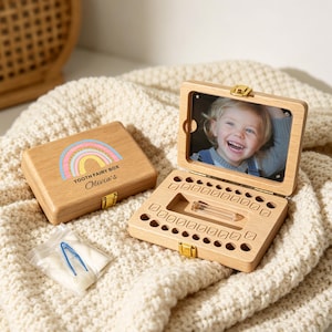 May include: A wooden tooth fairy box with a rainbow design and the text "Tooth Fairy Box Olivia's". The box is open, revealing a photo and compartments for teeth. A small bag with a blue tool is next to the box.