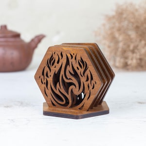 May include: Set of four wooden coasters with a hexagonal shape and a flame design. The coasters are made of dark brown wood and are stacked on a matching base. A brown teapot is visible in the background.