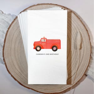 May include: White paper napkins featuring a red fire truck illustration with black wheels. The fire truck has a Dalmatian dog in the driver's seat and the text "CAMDEN'S 2ND BIRTHDAY" printed below the truck.